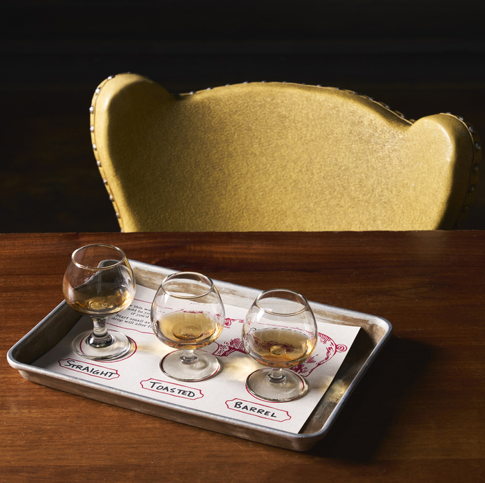 Golden tray with three glasses of whiskey on a table, labeled straight, toasted, and barrel.