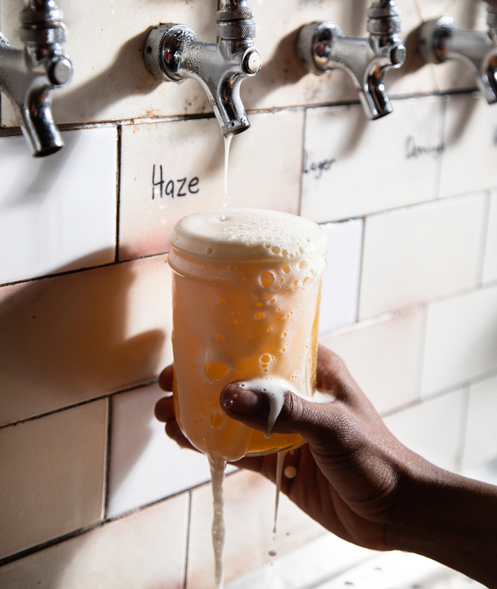 Person filling a cup with hazy beer from a tap.
