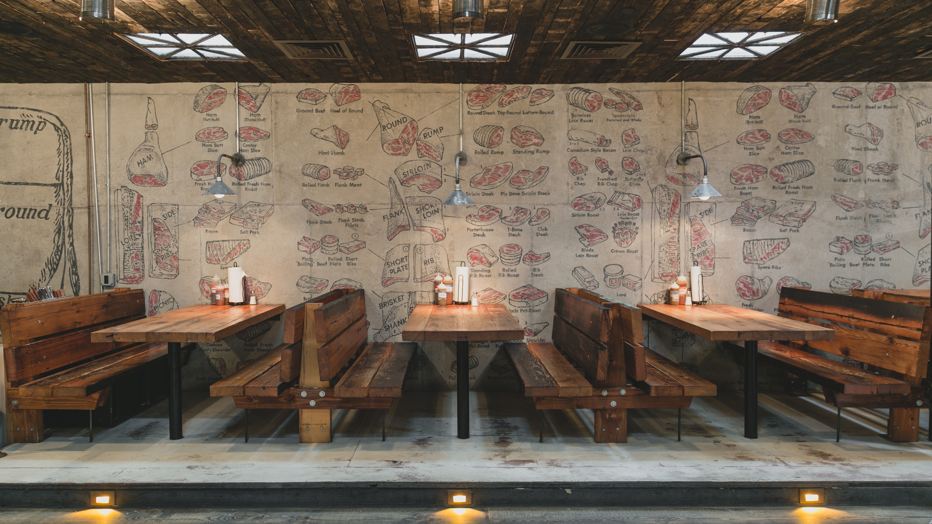 Wooden bench seating in a restaurant with industrial-style lights and a rustic wall mural.